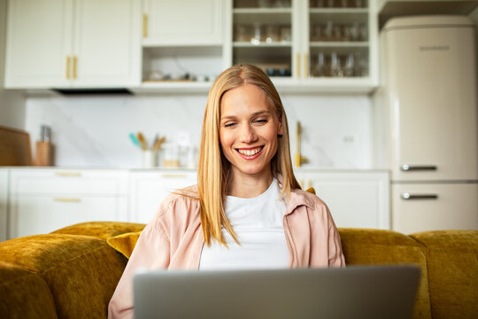 Smiling woman using laptop on sofa in kitchen