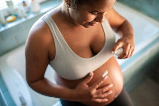 Pregnant woman applying lotion to belly in bathroom