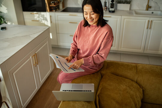 Smiling woman reviewing financial paperwork with laptop at home