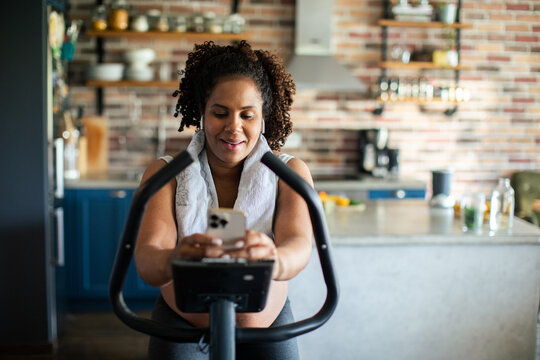 Woman on exercise bike using smartphone in home kitchen