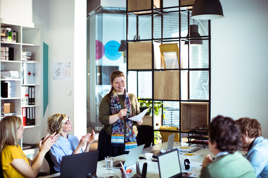 Team applauding woman giving presentation in modern office