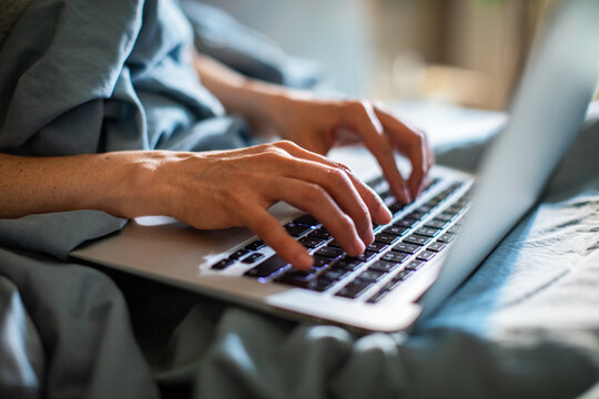 Close-up of hands typing on laptop in bed