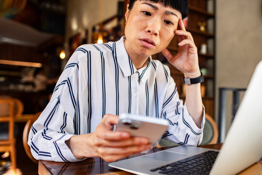 Concerned woman checking phone beside laptop in cafe