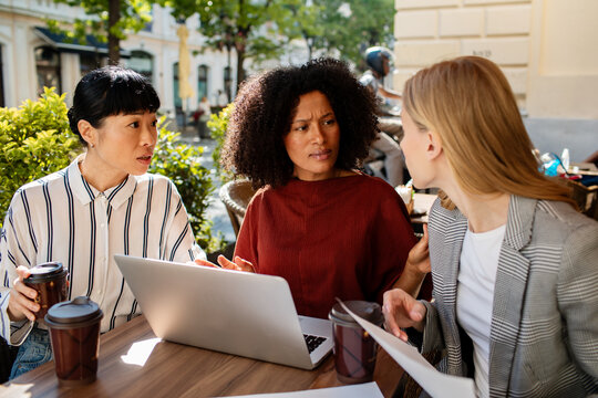 Three colleagues debating a document at an outdoor cafe