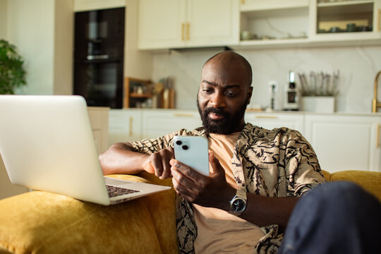 Man texting on smartphone with laptop at home