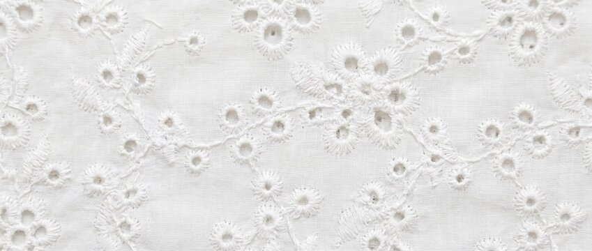 White broderie anglaise lace fabric texture. Cotton eyelet embroidery textile surface with floral pattern