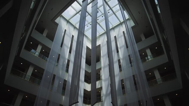 Swaying long fabric panels filling tall atrium with glass balconies, catching light from skylight