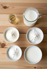 Fototapeta premium Plant based milk production, vegan dairy alternative ingredients with coconut flakes and oil in bowls on wooden table for healthy nutrition and cooking
