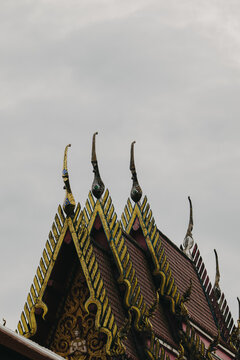 Traditional Thai temple roof decoration against cloudy sky.
