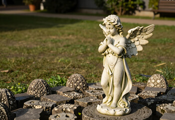 Fototapeta premium Spirituality and peace, stone angel statue praying in a garden setting with decorative paving stones for memorial or religious design concepts