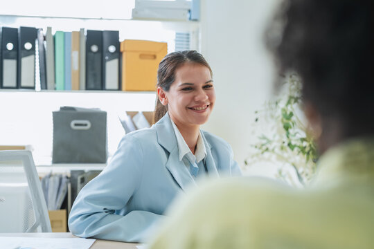 Smiling businesswoman talking with colleague across desk during friendly one on one meeting or job interview in office