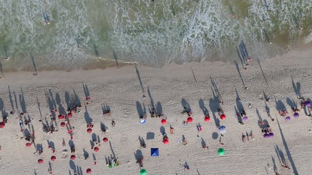Top-down aerial view of colorful umbrellas and beachgoers on Copacabana Beach as waves roll onto the sand, Rio de Janeiro, Brazil.