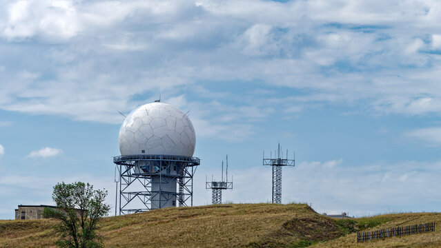 Panorama of a weather radar housed in a geodesic dome with other antennas on a hill