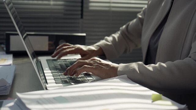 Businesswoman Typing on Laptop at Busy Office Desk with Documents