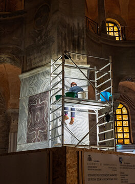 Eine nicht erkennbare Restauratorin arbeitet auf einem Ger&uuml;st konzentriert an einer S&auml;ule in der Basilica di San Vitale in Ravenna; 
