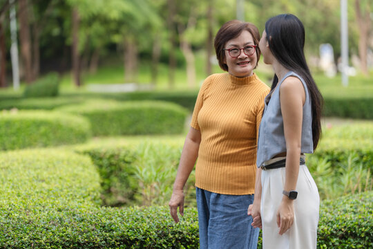 Happy Asian senior mother and adult daughter walking together in park and talking