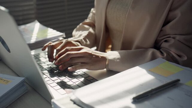 Businesswoman Typing on Laptop with Paperwork at Busy Office Desk
