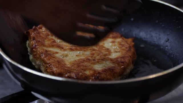 Flipping a crispy yellow split pea patty with wooden spatulas in a frying pan