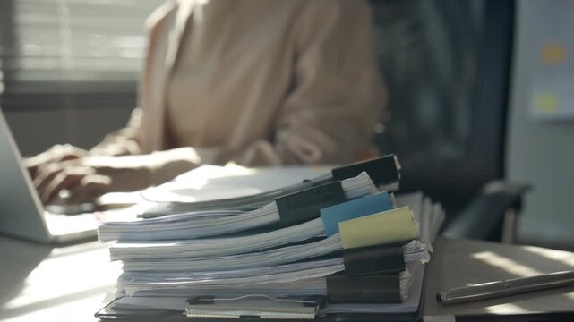 Overworked Businesswoman Working on Laptop Behind Stack of Office Documents