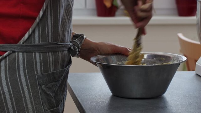 Woman stirring fresh yellow split pea patties dough with a wooden spoon in a metal bowl