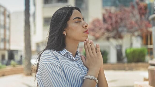 Woman with hands pressed together in prayer gesture beside building plaza; serenity devotion reflection.