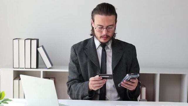 Businessman making an online payment with a credit card and smartphone while sitting in his modern office workspace