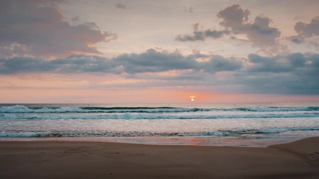 Beautiful sunrise over gentle sea waves rolling onto a sandy beach under soft pastel clouds during dawn.