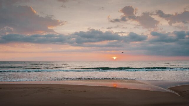 Beautiful sunrise over gentle sea waves rolling onto a sandy beach under soft pastel clouds during dawn.