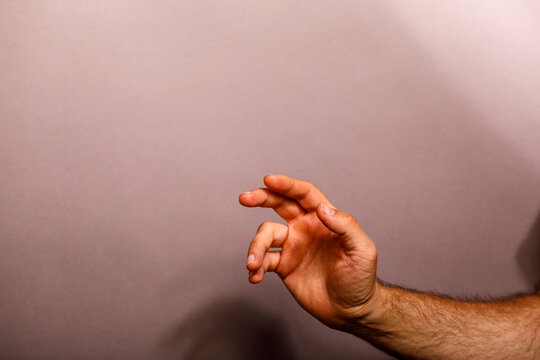A man's hand reaches out, fingers curled, against a simple pinkish-brown background.