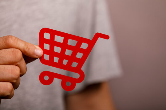 Close-up of a hand holding a vibrant red shopping cart symbol against a blurred background.