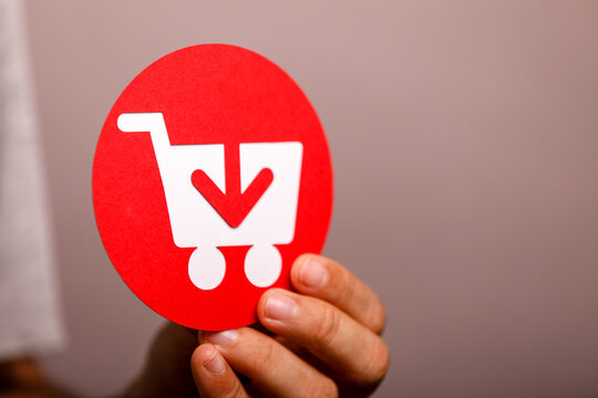 Hand holding a red shopping cart icon with a download arrow, representing online shopping.