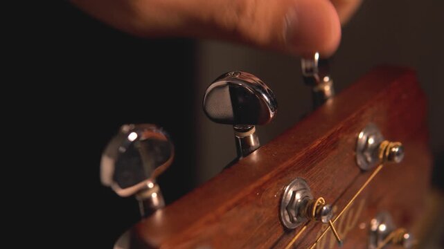 4K close-up shot of a man&rsquo;s hand tuning the knob of a wooden acoustic guitar for the strings. The concept of art, entertainment, creativity, and live performance.