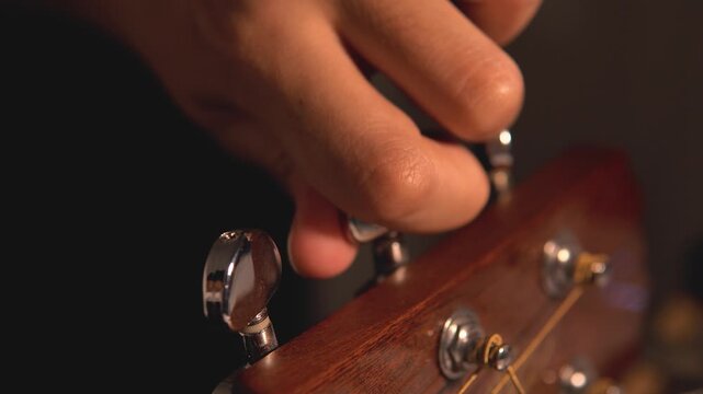 4K close-up shot of a man&rsquo;s hand tuning the knob of a wooden acoustic guitar for the strings. The concept of art, entertainment, creativity, and live performance.