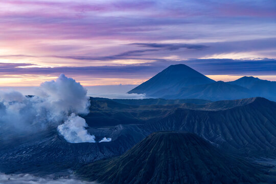 Mount Bromo volcano at sunrise, viewed from King Kong viewpoint in Bromo Tengger Semeru National Park, East Java, Indonesia. Active crater smoke, Mount Semeru cone, clouds, and vast ash plain.