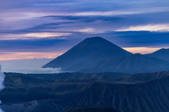 Mount Bromo volcano at sunrise, viewed from King Kong viewpoint in Bromo Tengger Semeru National Park, East Java, Indonesia. Active crater smoke, Mount Semeru cone, clouds, and vast ash plain.