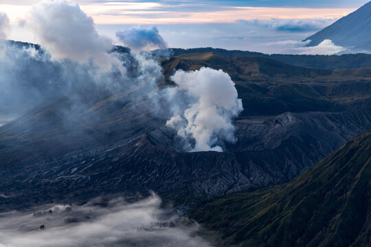 Mount Bromo volcano at sunrise, viewed from King Kong viewpoint in Bromo Tengger Semeru National Park, East Java, Indonesia. Active crater smoke, Mount Semeru cone, clouds, and vast ash plain.