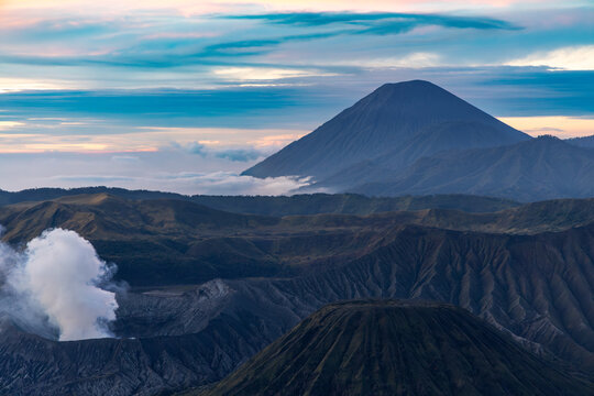 Mount Bromo volcano at sunrise, viewed from King Kong viewpoint in Bromo Tengger Semeru National Park, East Java, Indonesia. Active crater smoke, Mount Semeru cone, clouds, and vast ash plain.