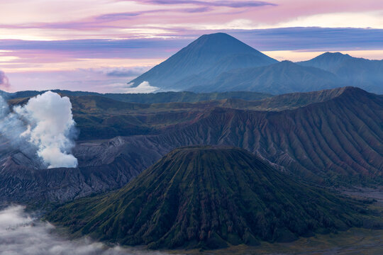 Mount Bromo volcano at sunrise, viewed from King Kong viewpoint in Bromo Tengger Semeru National Park, East Java, Indonesia. Active crater smoke, Mount Semeru cone, clouds, and vast ash plain.