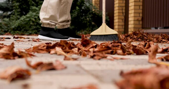 Autumn cleaning of the territory near the house. Sweeping fallen leaves from yard tiles