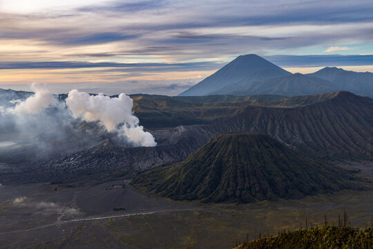 Mount Bromo volcano at sunrise, viewed from King Kong viewpoint in Bromo Tengger Semeru National Park, East Java, Indonesia. Active crater smoke, Mount Semeru cone, clouds, and vast ash plain.