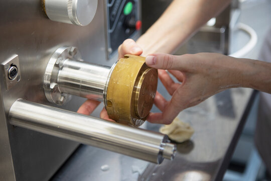 Hands attach brass die to stainless steel pasta extruder. Professional kitchen equipment for making macaroni. Food industry machine