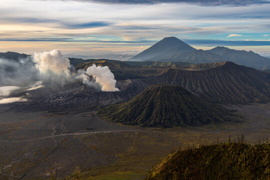 Mount Bromo volcano at sunrise, viewed from King Kong viewpoint in Bromo Tengger Semeru National Park, East Java, Indonesia. Active crater smoke, Mount Semeru cone, clouds, and vast ash plain.