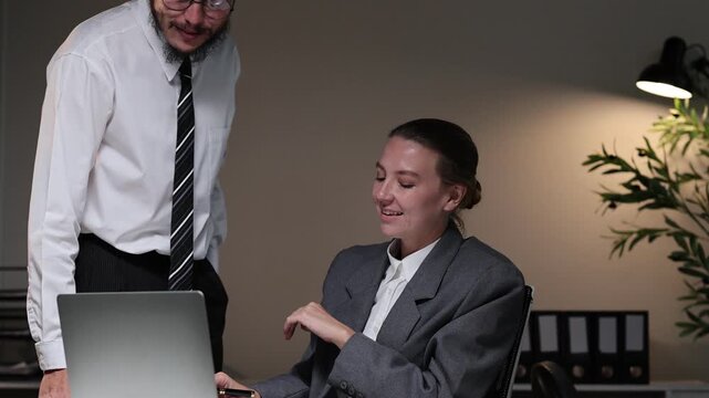 Angry male boss scolding and yelling at his young female employee for a mistake in the office late at night