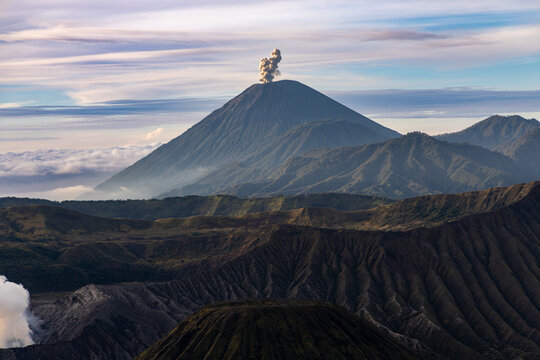 Mount Bromo volcano at sunrise, viewed from King Kong viewpoint in Bromo Tengger Semeru National Park, East Java, Indonesia. Active crater smoke, Mount Semeru cone, clouds, and vast ash plain.