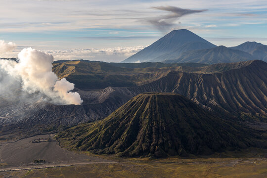 Mount Bromo volcano at sunrise, viewed from King Kong viewpoint in Bromo Tengger Semeru National Park, East Java, Indonesia. Active crater smoke, Mount Semeru cone, clouds, and vast ash plain.
