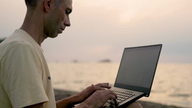 Remote work on laptop from pebble seashore with ocean waves at dusk