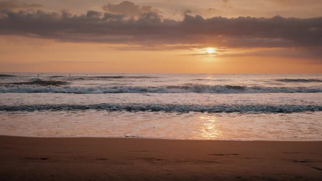 Gentle ocean waves rolling onto a sandy beach shore during a golden sunrise under soft cloudy sky.