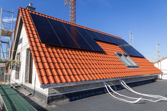 K&uuml;rzlich eingedecktes Ziegeldach mit Dachfenstern und Solarpaneelen an einem neuen Einfamilienhaus