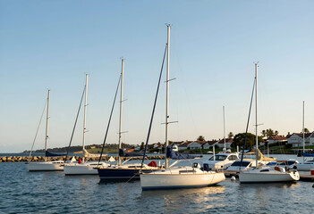 Obraz premium Leisure travel and luxury lifestyle, sailboats moored at a marina harbor during sunset with coastal residential homes in the background on a calm day