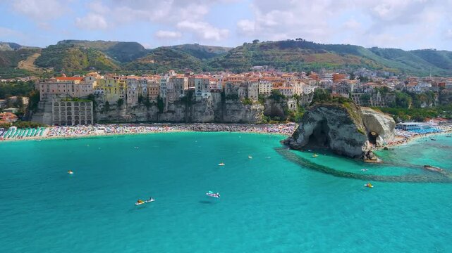 Tropea Calabria Italy 4k drone view of Santa Maria dell Isola sanctuary on rock. Flyover beach with colorful umbrellas between cliffs and clifftop town, summer resort establishing shot